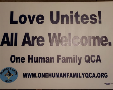 Picture of a yard sign that reads 'Love United! All Are Welcome. One Human Family QCA,' with the OHF QCA logo and the URL to their website.